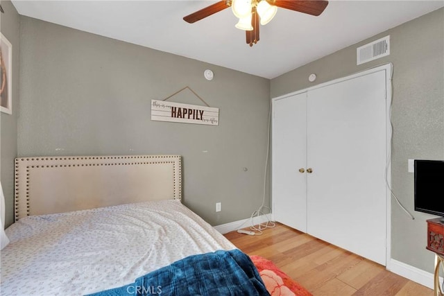 bedroom featuring a ceiling fan, wood finished floors, visible vents, baseboards, and a closet