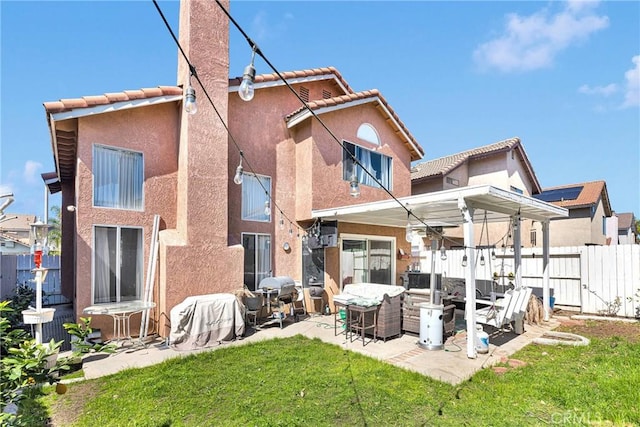 back of property with fence, a tile roof, stucco siding, a yard, and a patio area