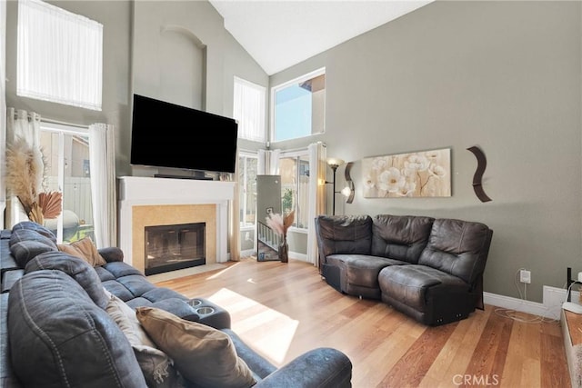 living area featuring a fireplace with flush hearth, high vaulted ceiling, baseboards, and wood finished floors