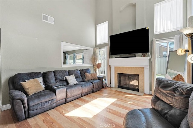 living room featuring a fireplace with flush hearth, wood finished floors, visible vents, and a towering ceiling