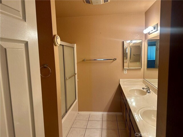 bathroom featuring tile patterned flooring, baseboards, bath / shower combo with glass door, double vanity, and a sink