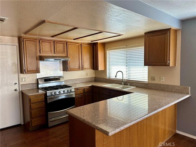 kitchen with stainless steel gas range oven, a sink, a textured ceiling, dark wood finished floors, and a peninsula