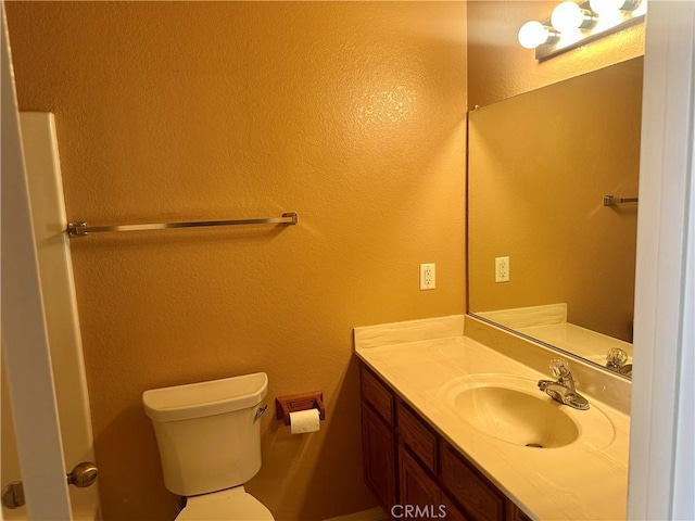 bathroom with toilet, vanity, and a textured wall