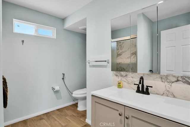 bathroom with a marble finish shower, backsplash, toilet, wood finished floors, and vanity