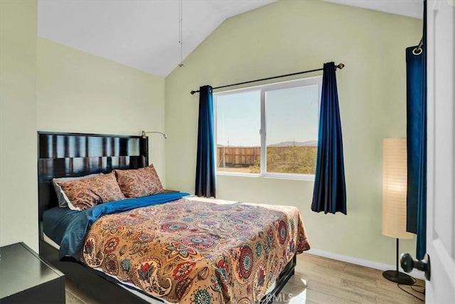 bedroom with vaulted ceiling, wood finished floors, and baseboards