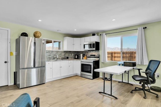 kitchen featuring white cabinetry, backsplash, light wood-type flooring, and appliances with stainless steel finishes