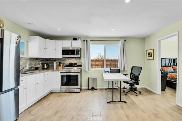 kitchen with stainless steel appliances, white cabinets, decorative backsplash, and light wood finished floors