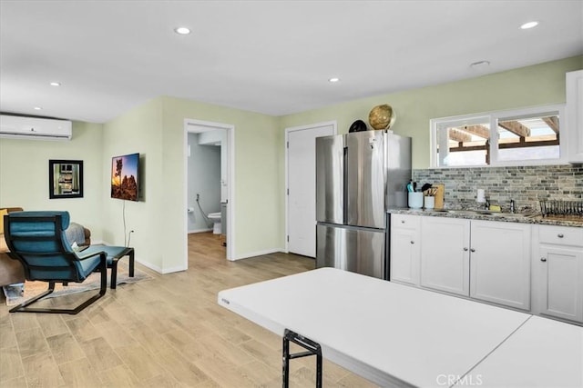 kitchen featuring a wall mounted AC, light wood-style flooring, freestanding refrigerator, decorative backsplash, and white cabinetry