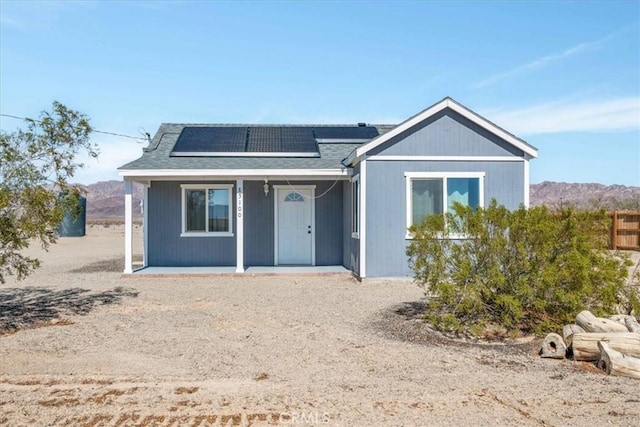 view of front facade featuring a mountain view, roof mounted solar panels, and a shingled roof