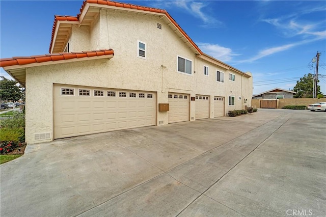 view of side of property with stucco siding, a tile roof, a garage, and fence