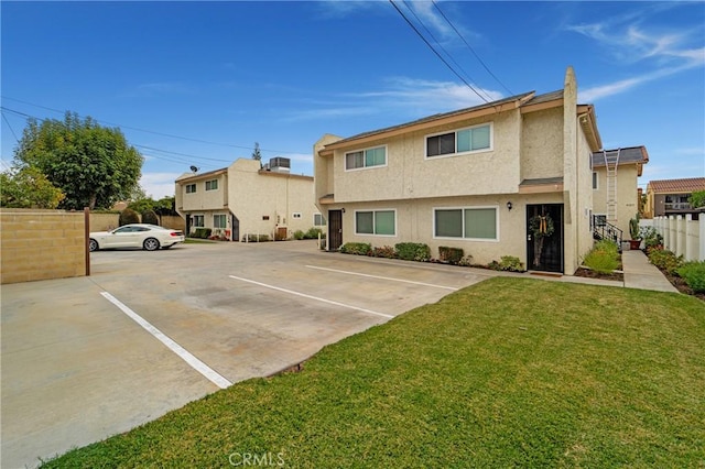 back of house with stucco siding, a yard, uncovered parking, and fence