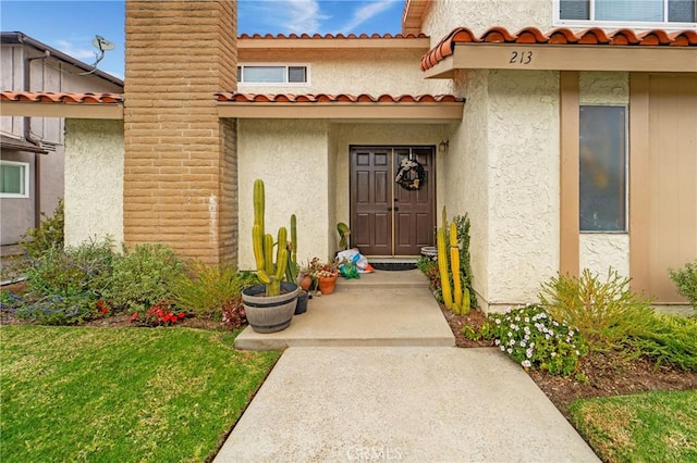 entrance to property with a tile roof, a chimney, and stucco siding