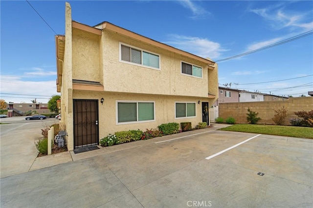 view of front of property featuring stucco siding, uncovered parking, and fence