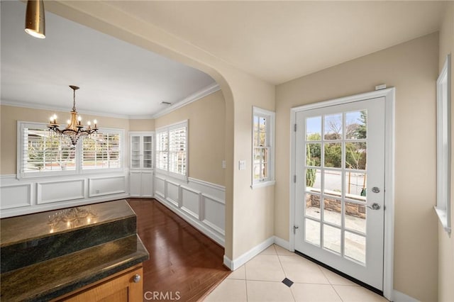 entryway with crown molding, a decorative wall, a notable chandelier, and a wealth of natural light