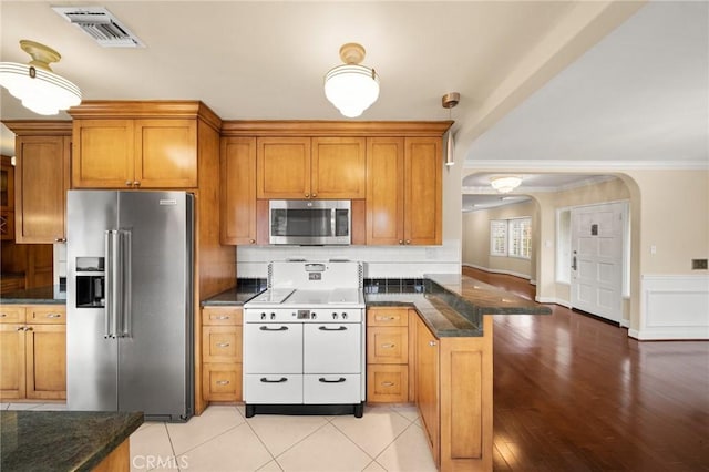 kitchen with brown cabinetry, visible vents, a peninsula, arched walkways, and stainless steel appliances