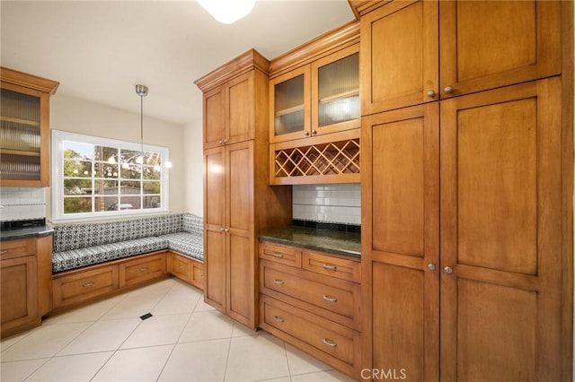 kitchen with decorative backsplash, glass insert cabinets, decorative light fixtures, and brown cabinetry