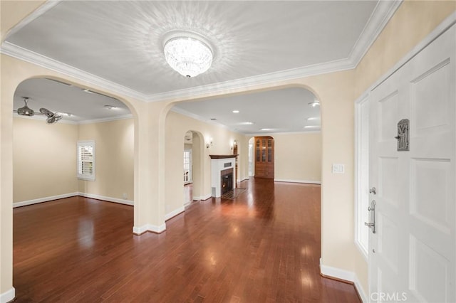 foyer featuring crown molding, baseboards, a lit fireplace, wood finished floors, and arched walkways