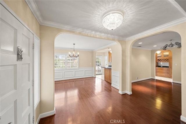 unfurnished dining area featuring a notable chandelier, dark wood-type flooring, arched walkways, crown molding, and a decorative wall