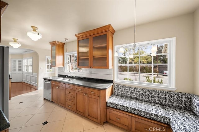 kitchen featuring arched walkways, stainless steel dishwasher, brown cabinetry, and a sink