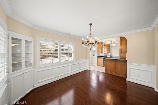 unfurnished dining area with dark wood finished floors, an inviting chandelier, a wainscoted wall, and arched walkways