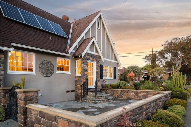 view of front of property featuring stone siding, stucco siding, roof mounted solar panels, and roof with shingles