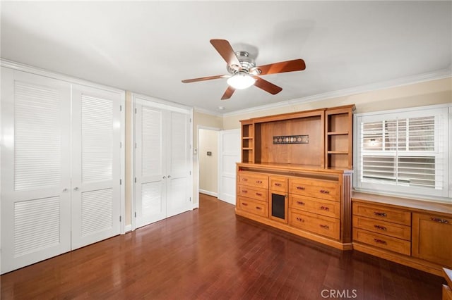 unfurnished bedroom featuring a ceiling fan, multiple closets, dark wood-style flooring, and ornamental molding