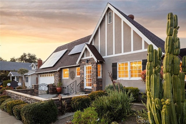 tudor-style house with solar panels, a garage, stone siding, and stucco siding