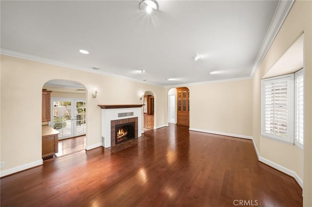 unfurnished living room featuring a fireplace, wood finished floors, arched walkways, and ornamental molding