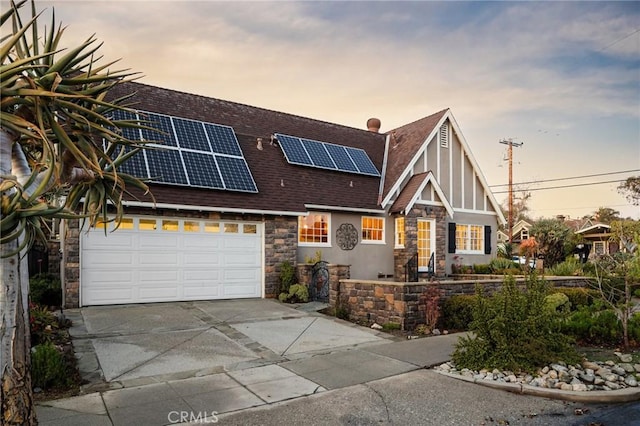 view of front of home featuring driveway, solar panels, an attached garage, stucco siding, and stone siding