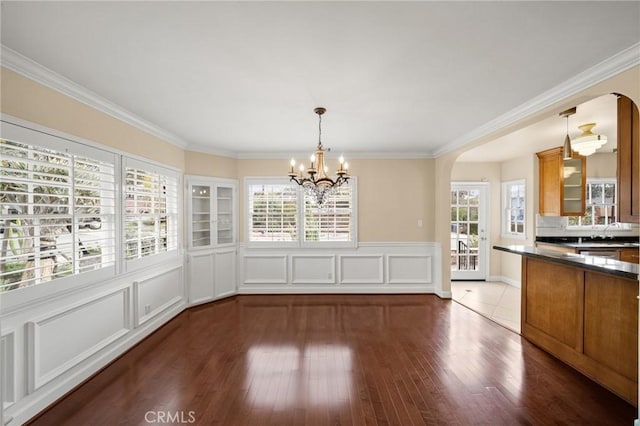 unfurnished dining area featuring arched walkways, a decorative wall, crown molding, and wood finished floors