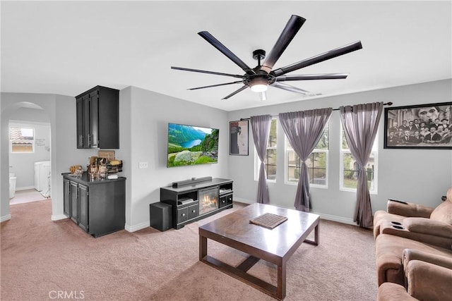 living area featuring arched walkways, light carpet, baseboards, and a ceiling fan