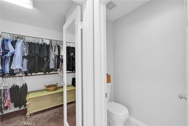 bathroom featuring visible vents, toilet, a walk in closet, and baseboards