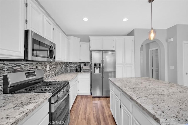 kitchen featuring tasteful backsplash, white cabinetry, arched walkways, light wood-style floors, and appliances with stainless steel finishes