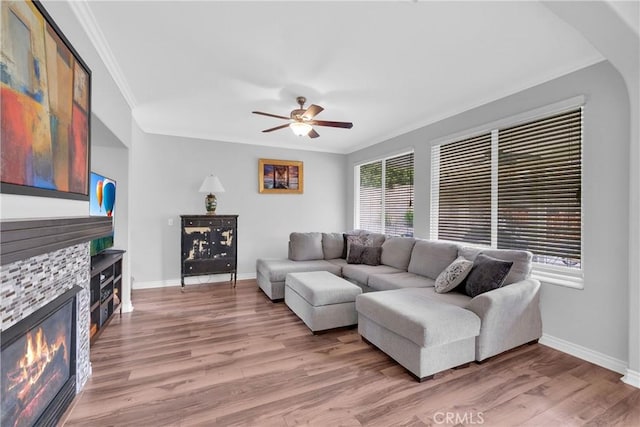 living room with a glass covered fireplace, light wood-style flooring, baseboards, and ornamental molding