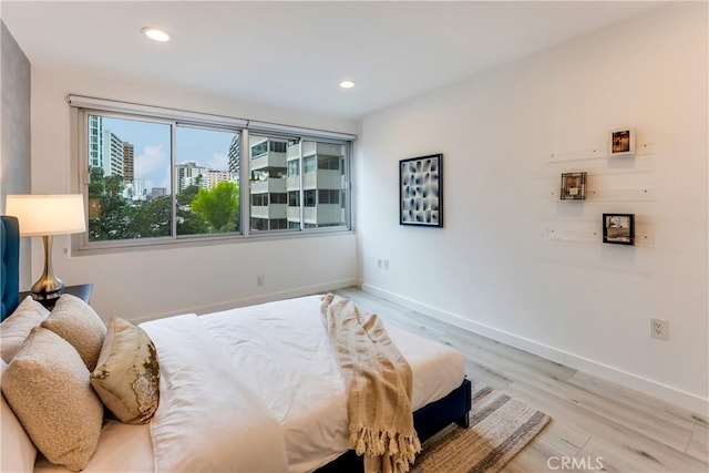 bedroom featuring recessed lighting, light wood-type flooring, a view of city, and baseboards