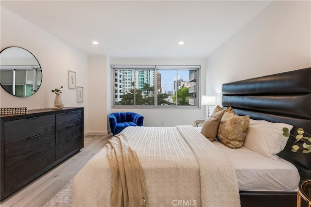 bedroom featuring light wood finished floors, a city view, and recessed lighting