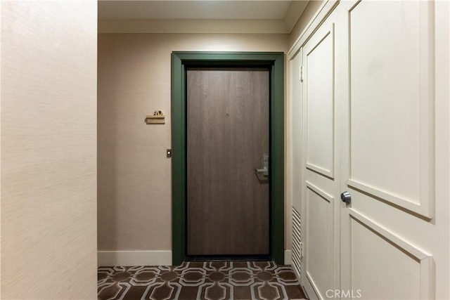 doorway with baseboards and dark tile patterned flooring