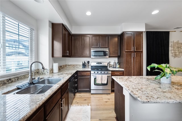 kitchen with light stone counters, light wood-style flooring, a sink, stainless steel appliances, and dark brown cabinetry