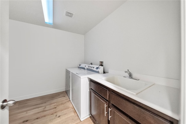 clothes washing area with visible vents, cabinet space, a sink, washing machine and dryer, and light wood-type flooring