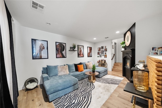 living room with a glass covered fireplace, visible vents, light wood-style flooring, and recessed lighting