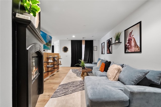 living area featuring recessed lighting, light wood-type flooring, and a warm lit fireplace