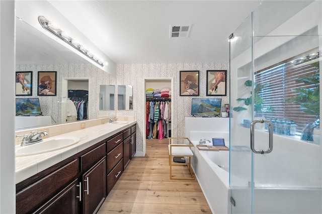 bathroom featuring visible vents, wallpapered walls, double vanity, a sink, and a bath