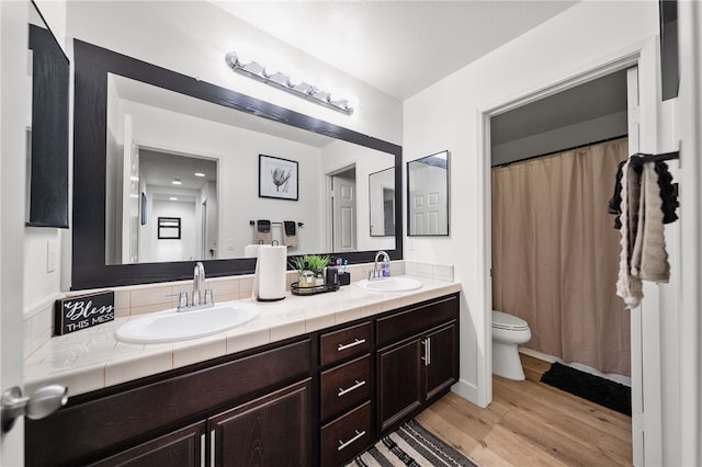 bathroom with double vanity, toilet, wood finished floors, and a sink