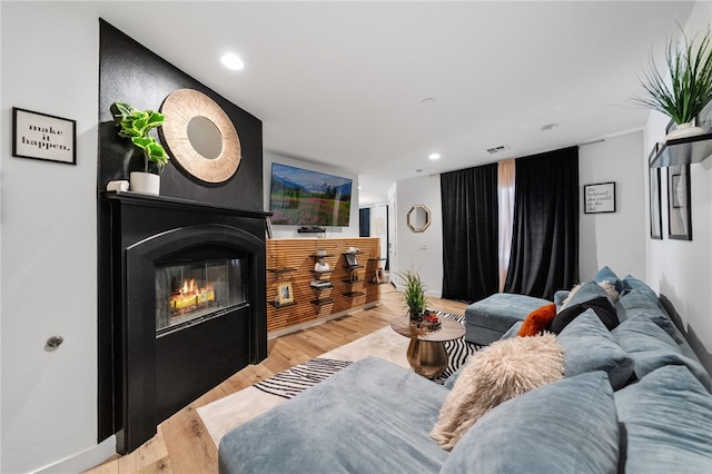 living area featuring recessed lighting, light wood-type flooring, baseboards, and a glass covered fireplace