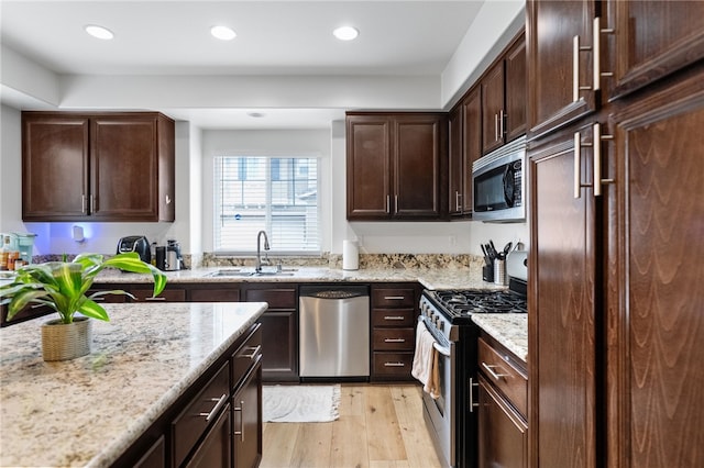 kitchen featuring light stone countertops, a sink, stainless steel appliances, dark brown cabinetry, and light wood-style floors