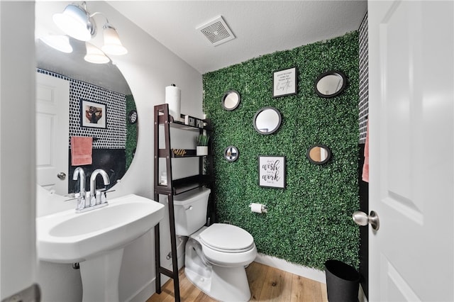 half bathroom with wood finished floors, visible vents, a sink, a textured ceiling, and toilet