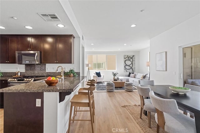 kitchen featuring visible vents, dark brown cabinetry, open floor plan, light wood-style floors, and stainless steel appliances