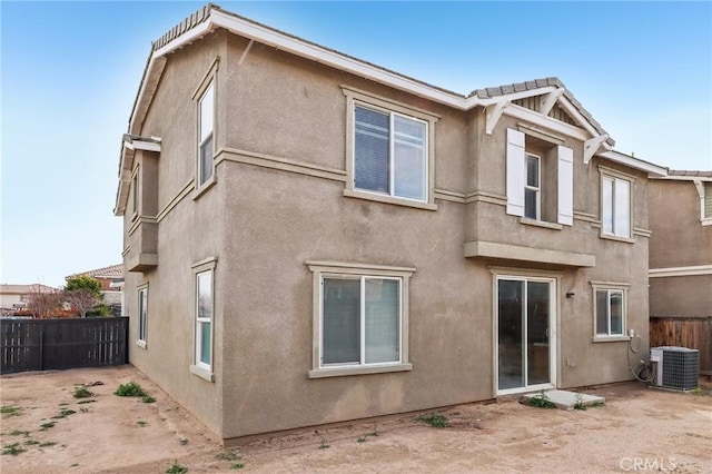 rear view of house with central air condition unit, stucco siding, and fence