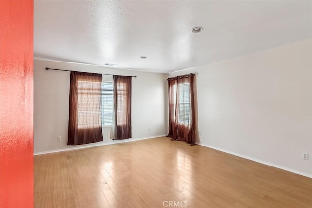 empty room featuring wood finished floors, visible vents, and baseboards