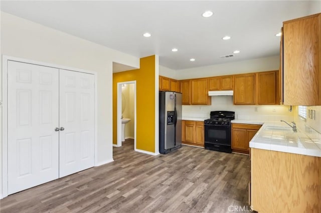 kitchen featuring black range with gas stovetop, under cabinet range hood, tile countertops, stainless steel fridge, and a sink